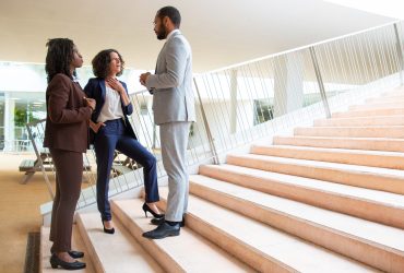 Business team on steps Business team on steps. Serious professional multiethnic business people standing and talking inside office building. Cooperation concept